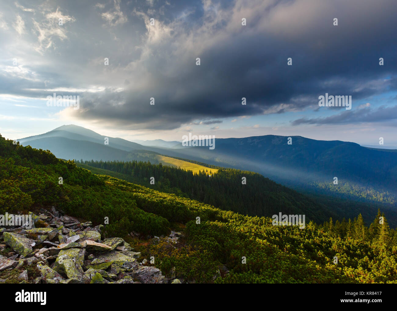 Last sun rays in evening sky with clouds above Syniak mountain. Summer sunset view from Homiak mountain, Gorgany, Carpathian, Ukraine. Stock Photo