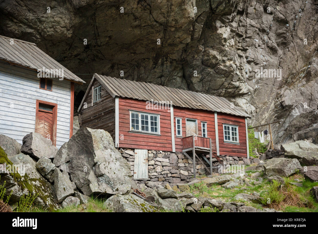 Abandoned old wooden houses dating back to the 1800s stand under a huge overhanging rock called Helleren forming a natural roof - Jossingfjord, Norway Stock Photo