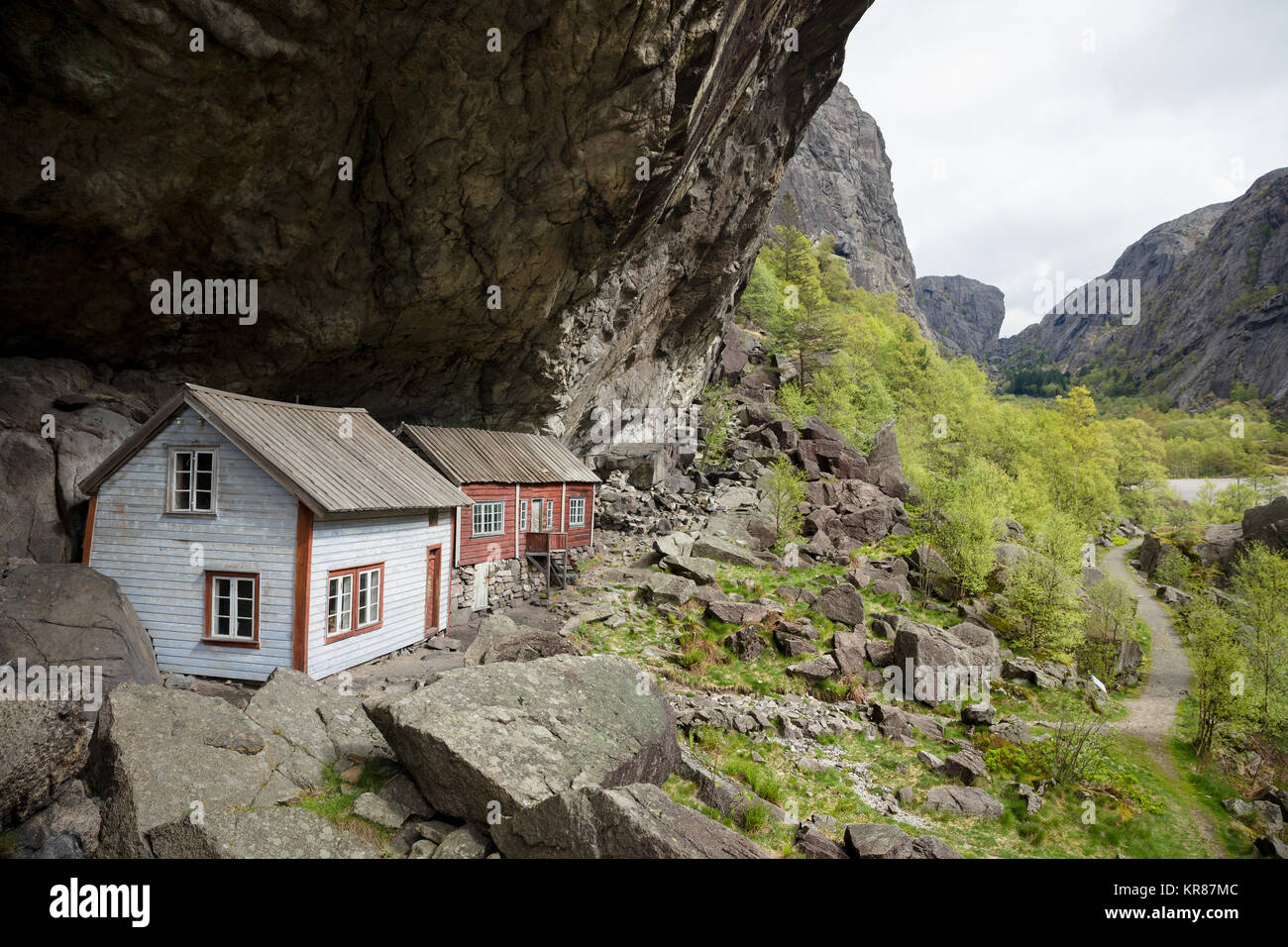 Abandoned old wooden houses dating back to the 1800s stand under a huge overhanging rock called Helleren forming a natural roof - Jossingfjord, Norway Stock Photo