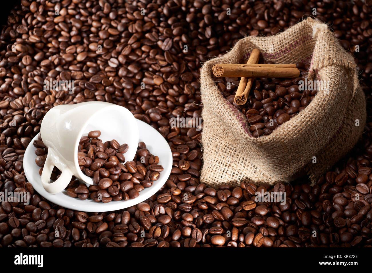 Studio Shot of White Cup of Coffee and Burlap Bag of Coffee over coffee beans and Cinammon Stock Photo