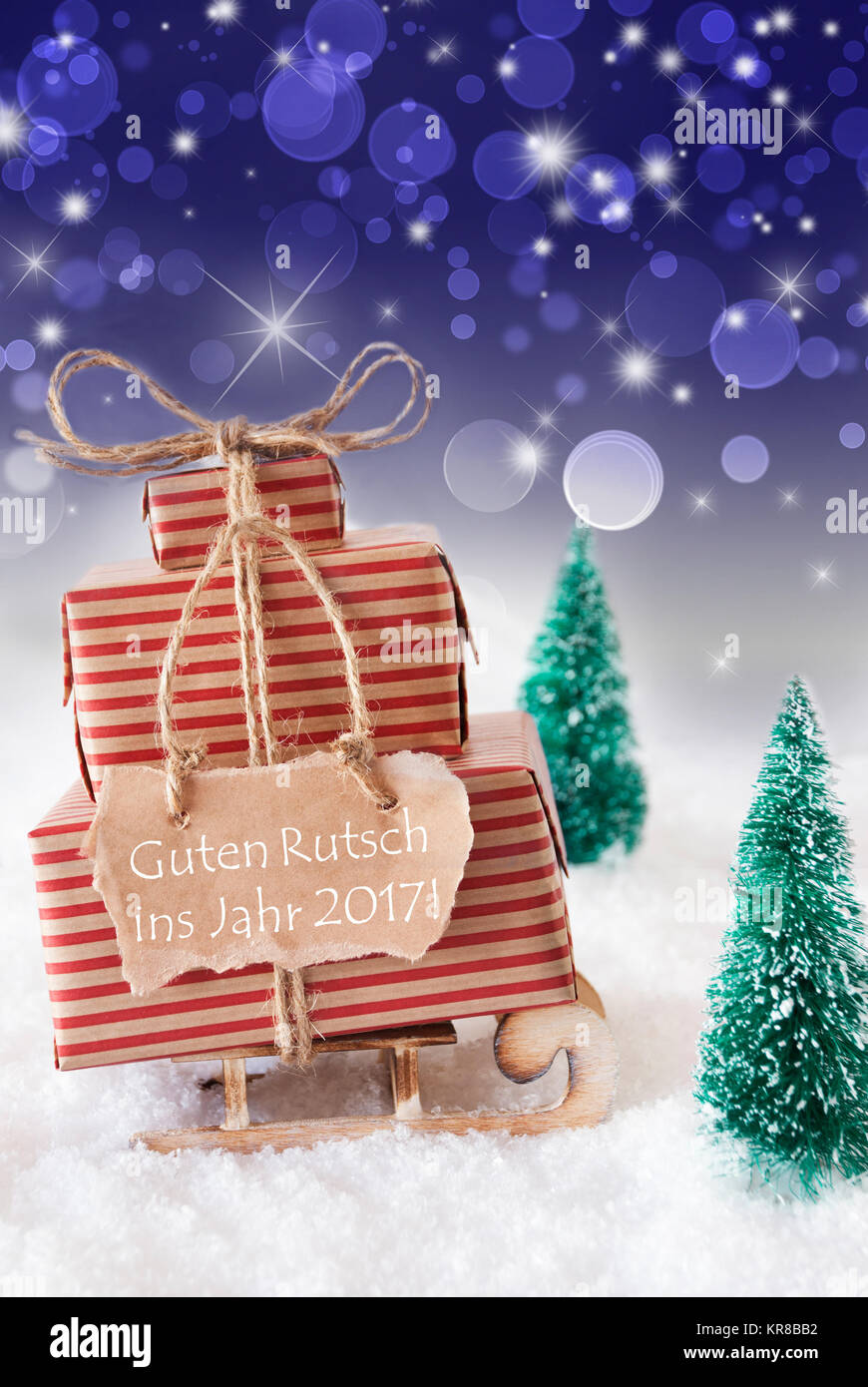 Vertical Image Of Sleigh Or Sled With Christmas Gifts, Snow And Trees. Blue Sparkling Background With Bokeh. Label With German Text Guten Rutsch Ins Jahr 2017 Means Happy New Year Stock Photo