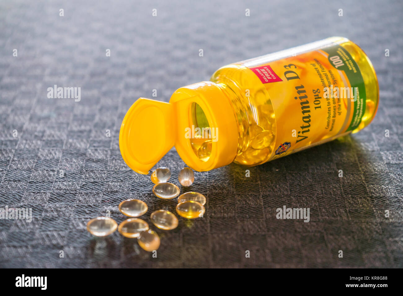 An open bottle of Vitamin D (D3) supplement pills/ tablets against grey background Stock Photo