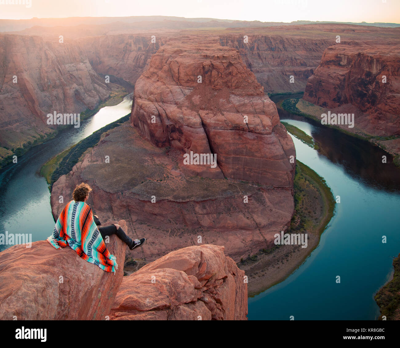 young man sitting on rock ledge over looking the horseshoe bend in Arizona, united states during sunset Stock Photo