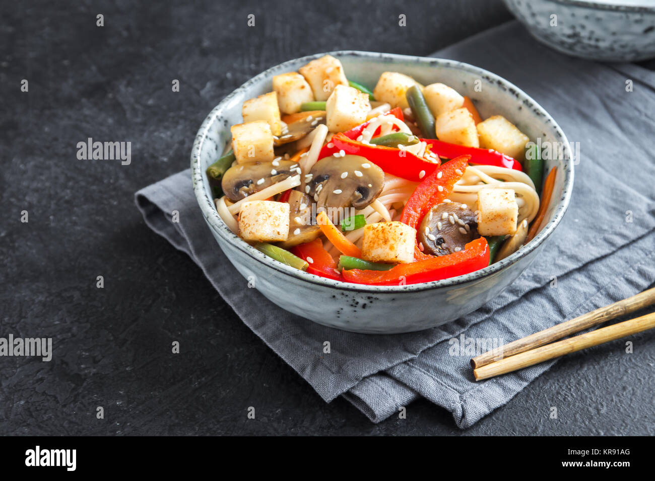 Stir fry with udon noodles, tofu, mushrooms and vegetables. Asian vegan vegetarian food, meal, stir fry over black background close up. Stock Photo