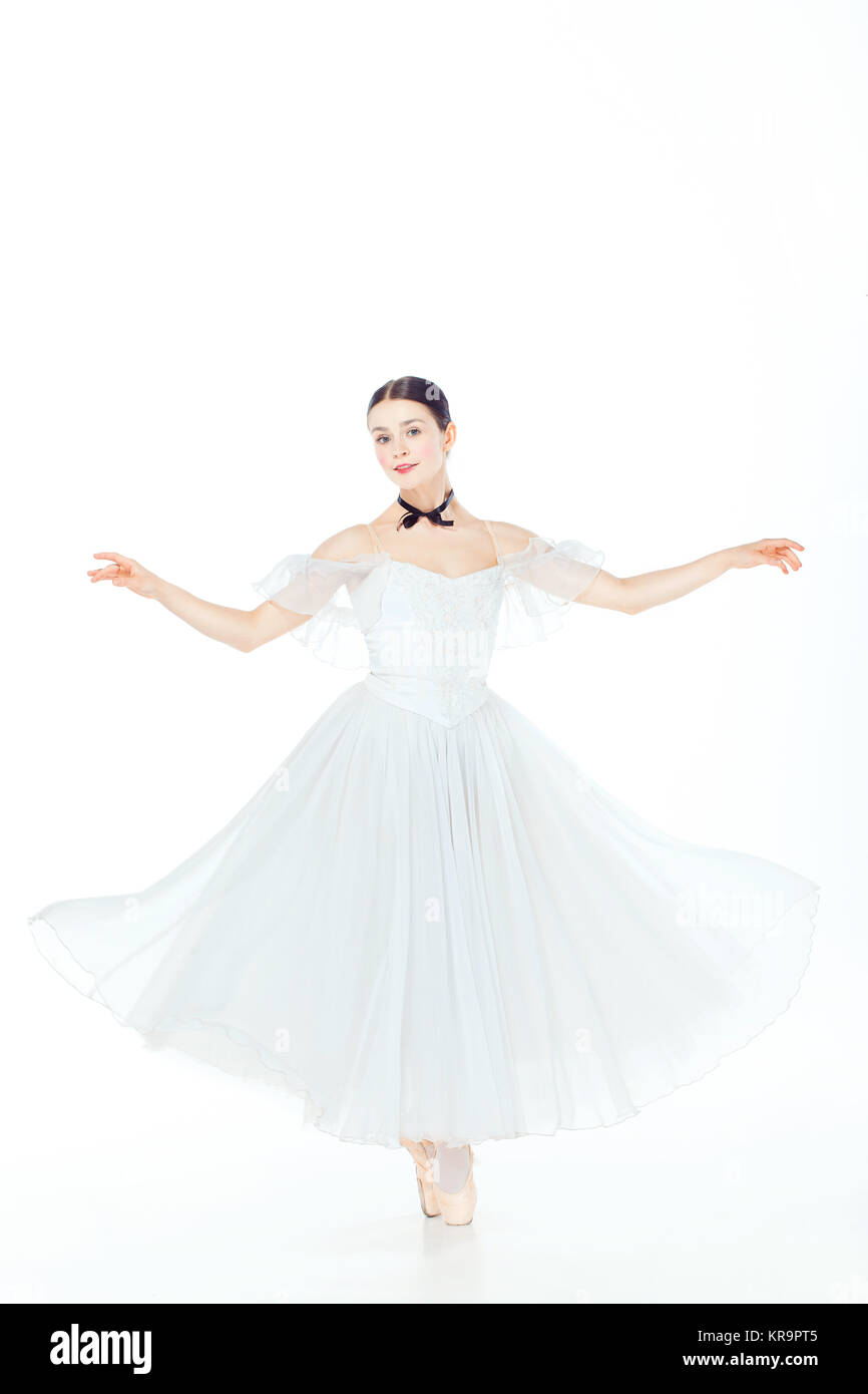 Ballerina in white dress posing on pointe shoes, studio background