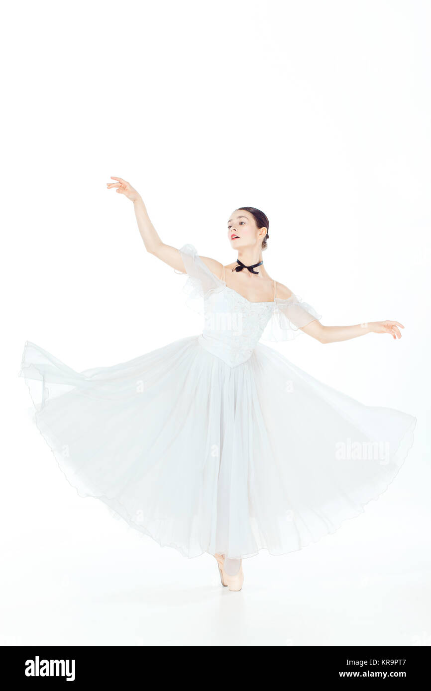 Ballerina in white dress posing on pointe shoes, studio background