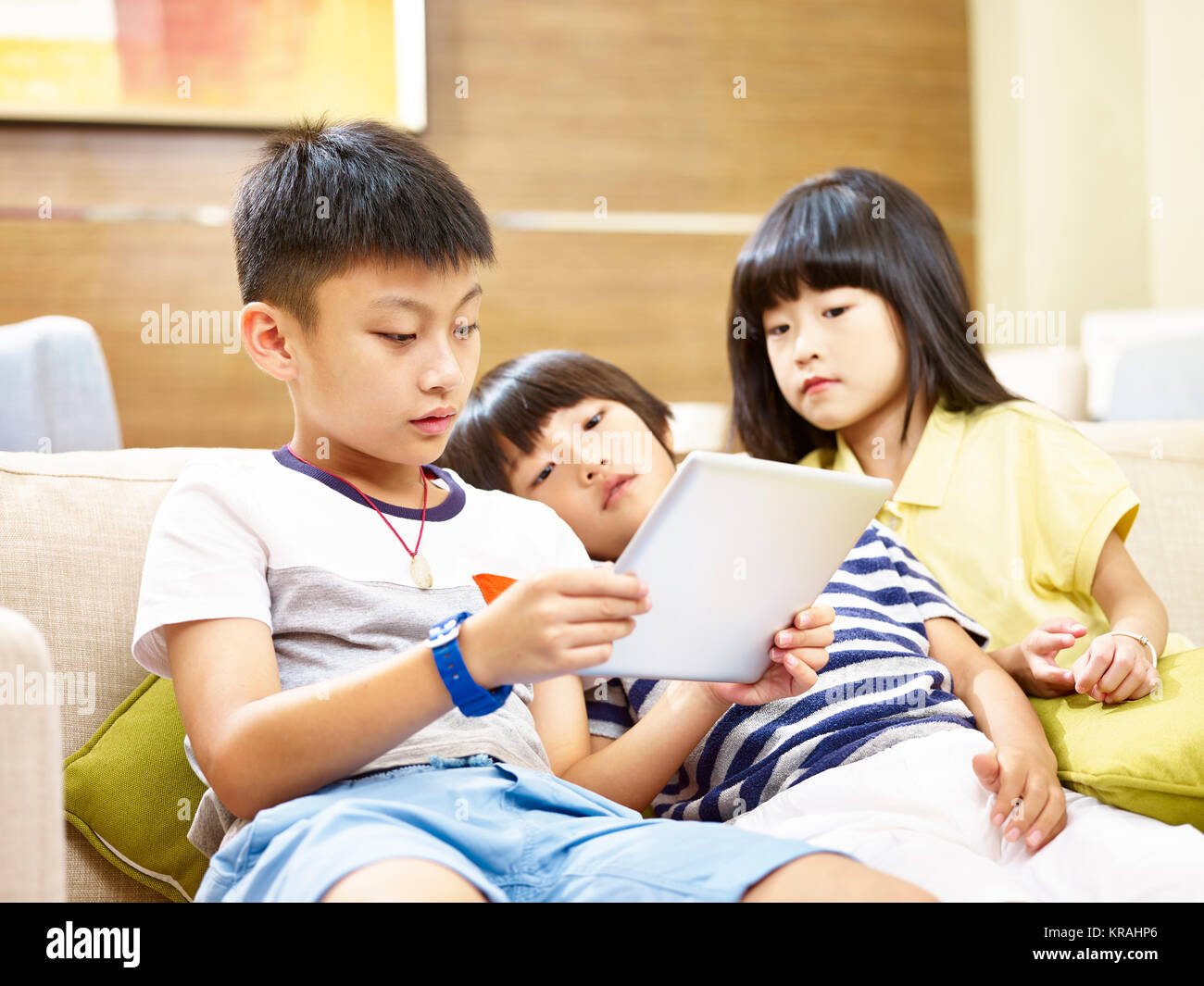 three asian children two little boy and one little girl lying on couch lazily playing video game with digital tablet. Stock Photo