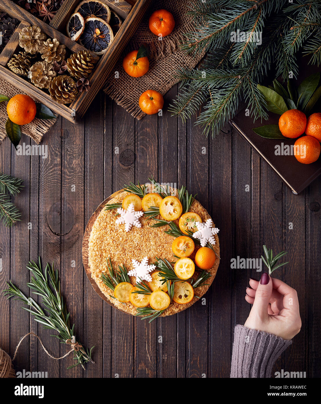 Woman decorates Christmas Honey cake with rosemary and oranges on brown wooden background. Stock Photo