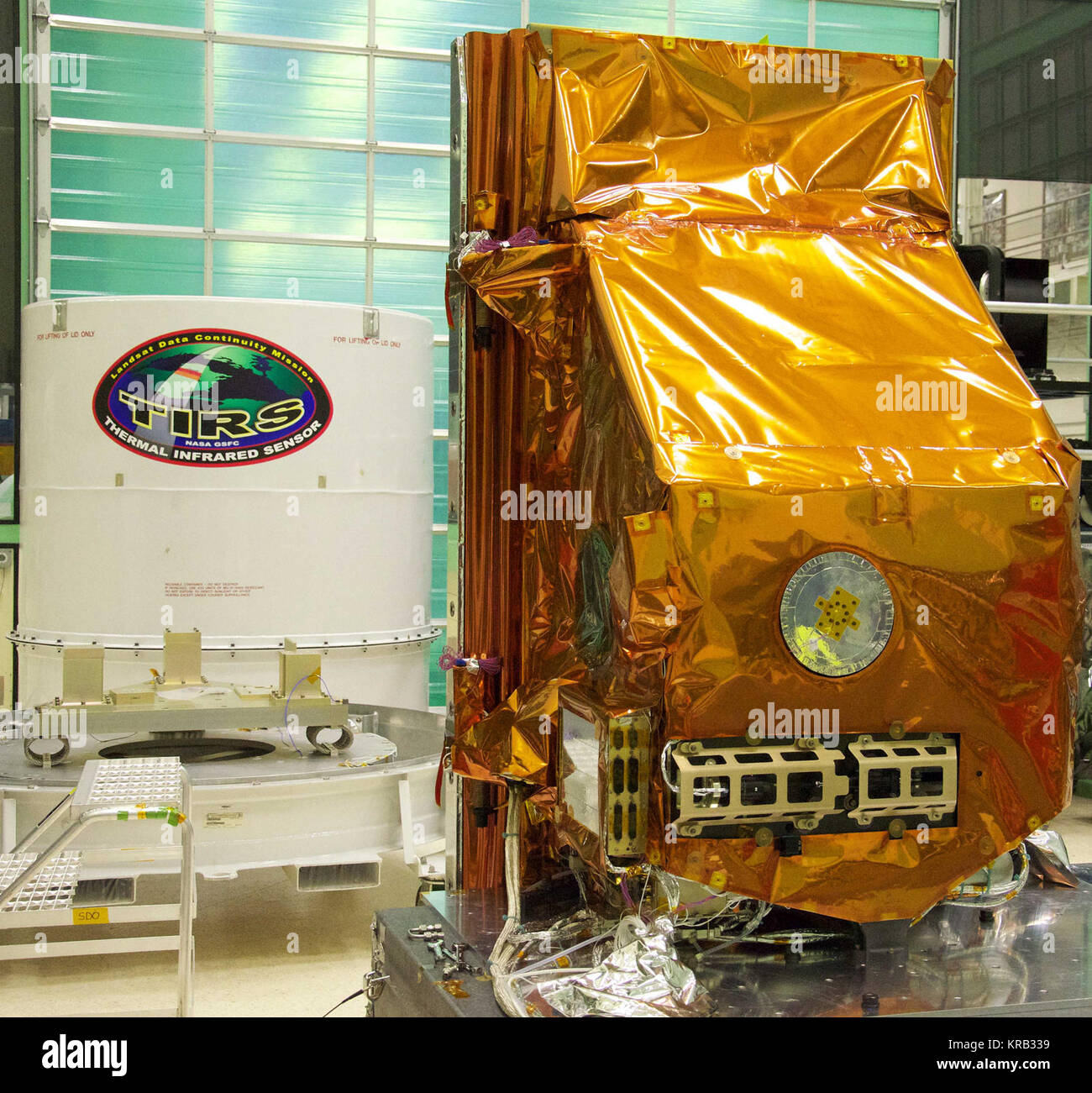 The TIRS instrument in the foreground with its shipping container waits in the background. The copper-color of TIRS is due to the gold-colored foil that coats the Multi-Layer Insulation blankets.  The Thermal Infrared Sensor (TIRS) will fly on the next Landsat satellite, the Landsat Data Continuity Mission (LDCM).  TIRS was built on an accelerated schedule at NASA's Goddard Space Flight Center, Greenbelt, Md. and will now be integrated into the LDCM spacecraft at Orbital Science Corp. in Gilbert, Ariz.   The Landsat Program is a series of Earth observing satellite missions jointly managed by N Stock Photo