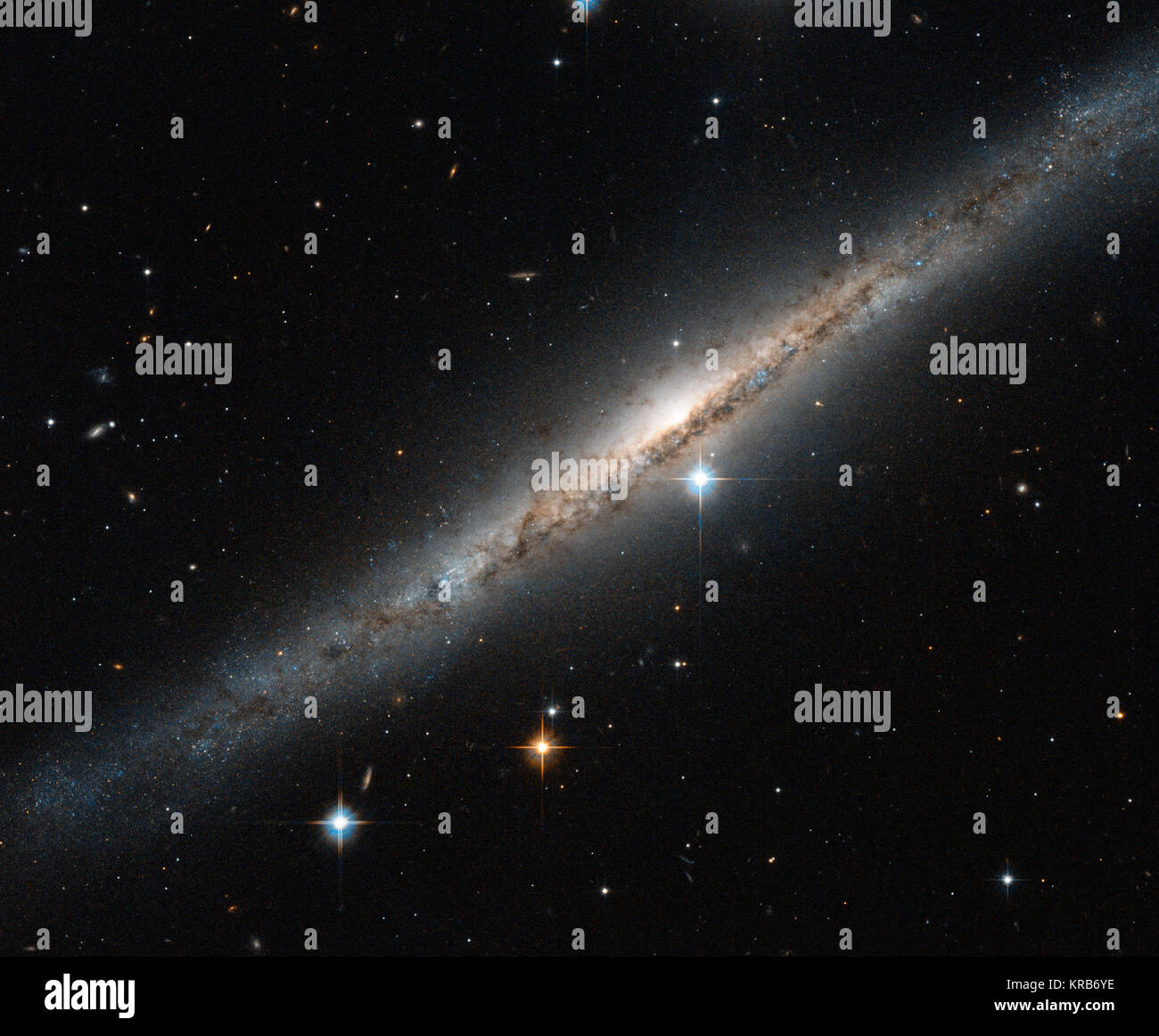 This  thin, glittering streak of stars is the spiral galaxy ESO 121-6, which  lies in the southern constellation of Pictor (The Painter's Easel).  Viewed almost exactly side-on, the intricate structure of the swirling  arms is hidden, but the full length of the galaxy can be seen —  including the intense glow from the central bulge, a dense region of  tightly packed young stars sitting at the centre of the spiral arms. Tendrils  of dark dust can be seen across the frame, partially obscuring the  bright centre of the galaxy and continuing out towards the smattering of  stars at its edges, where Stock Photo