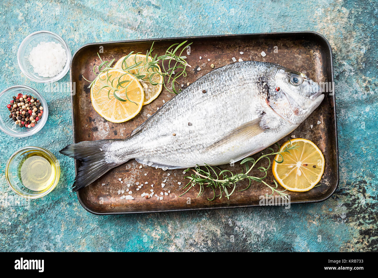 Fresh uncooked dorado or sea bream fish on tray with lemon slices and herbs over blue background, top view Stock Photo