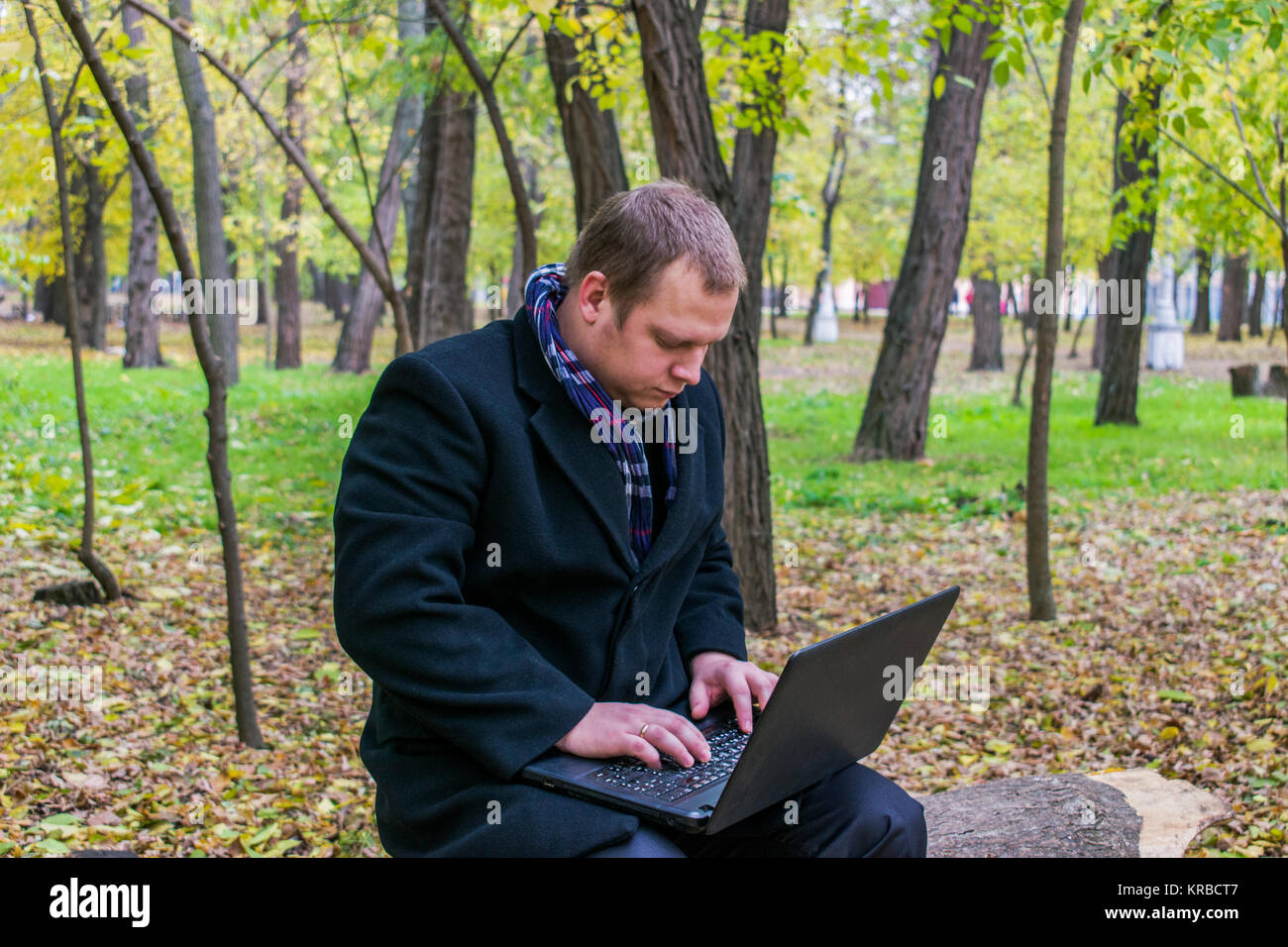Businessman having a laptop in the park in the fall. Young man sitting ...