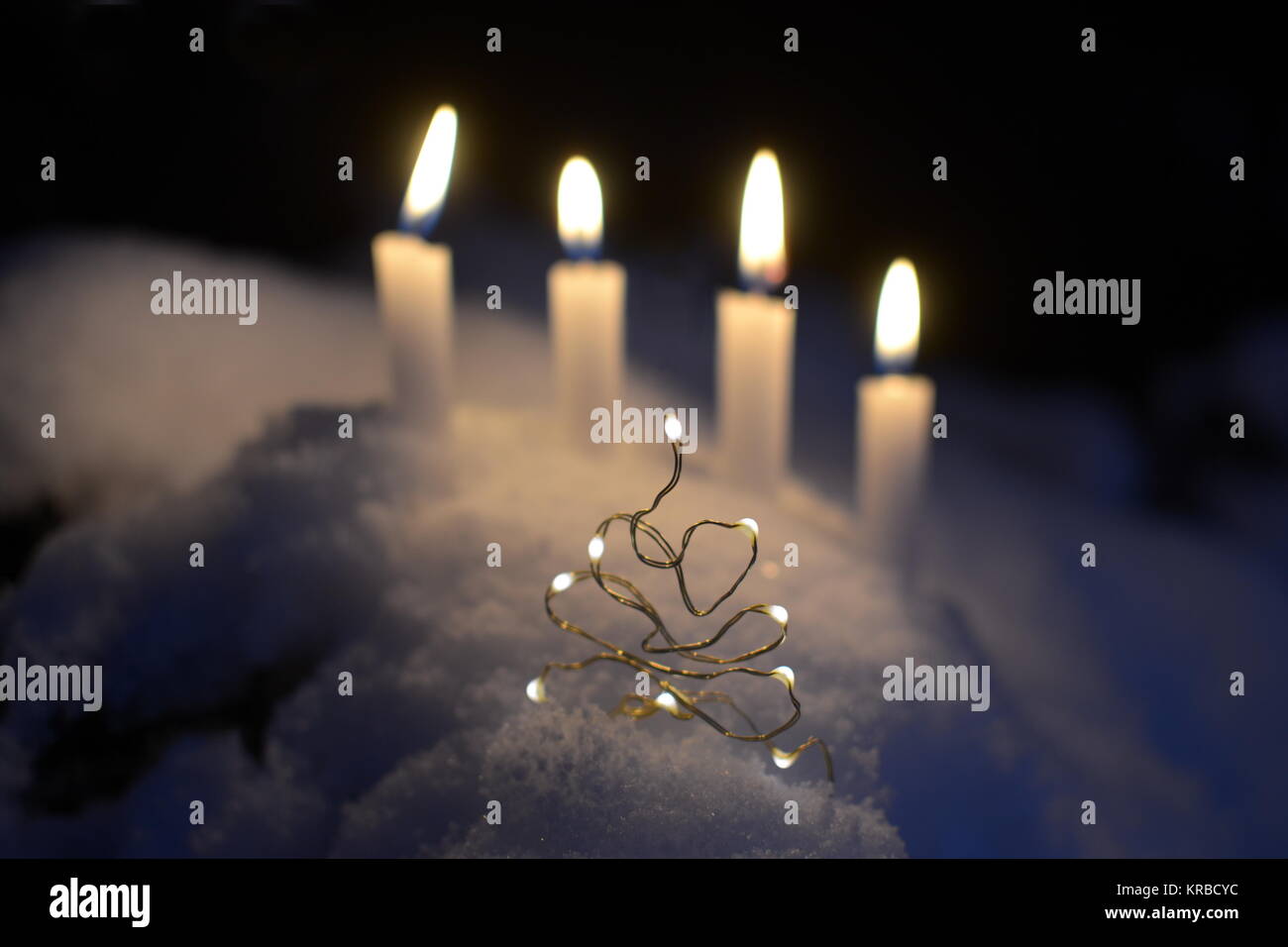 A little christmas tree with four white burning candles in the background, outdoors in the snow Stock Photo