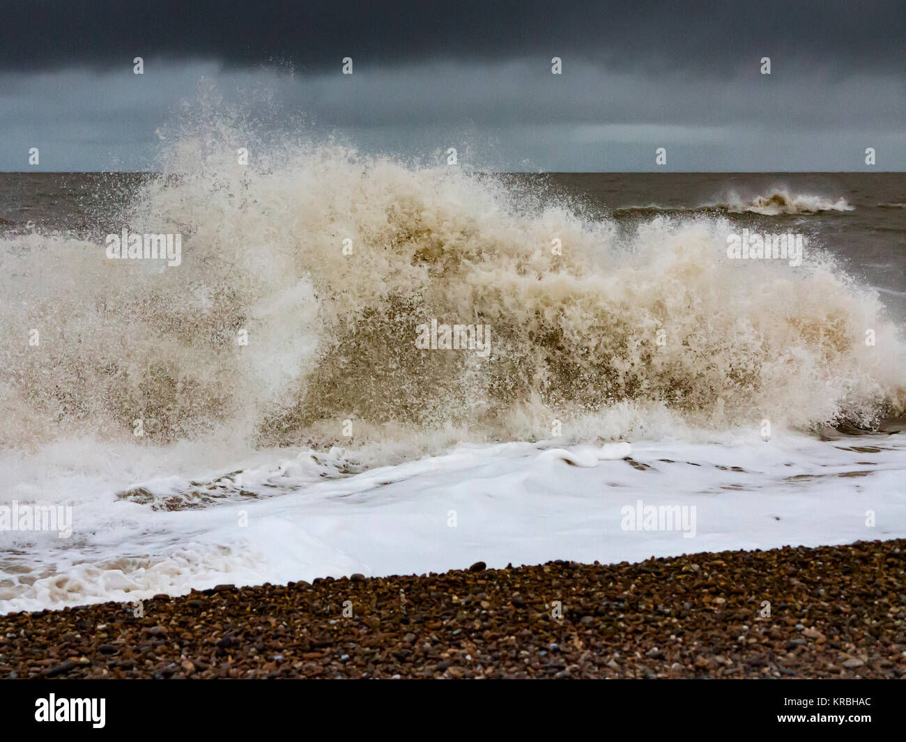 Churning waves breaking on the shoreline during heavy winds and spray with foam in the foreground against a dark angry sky Stock Photo