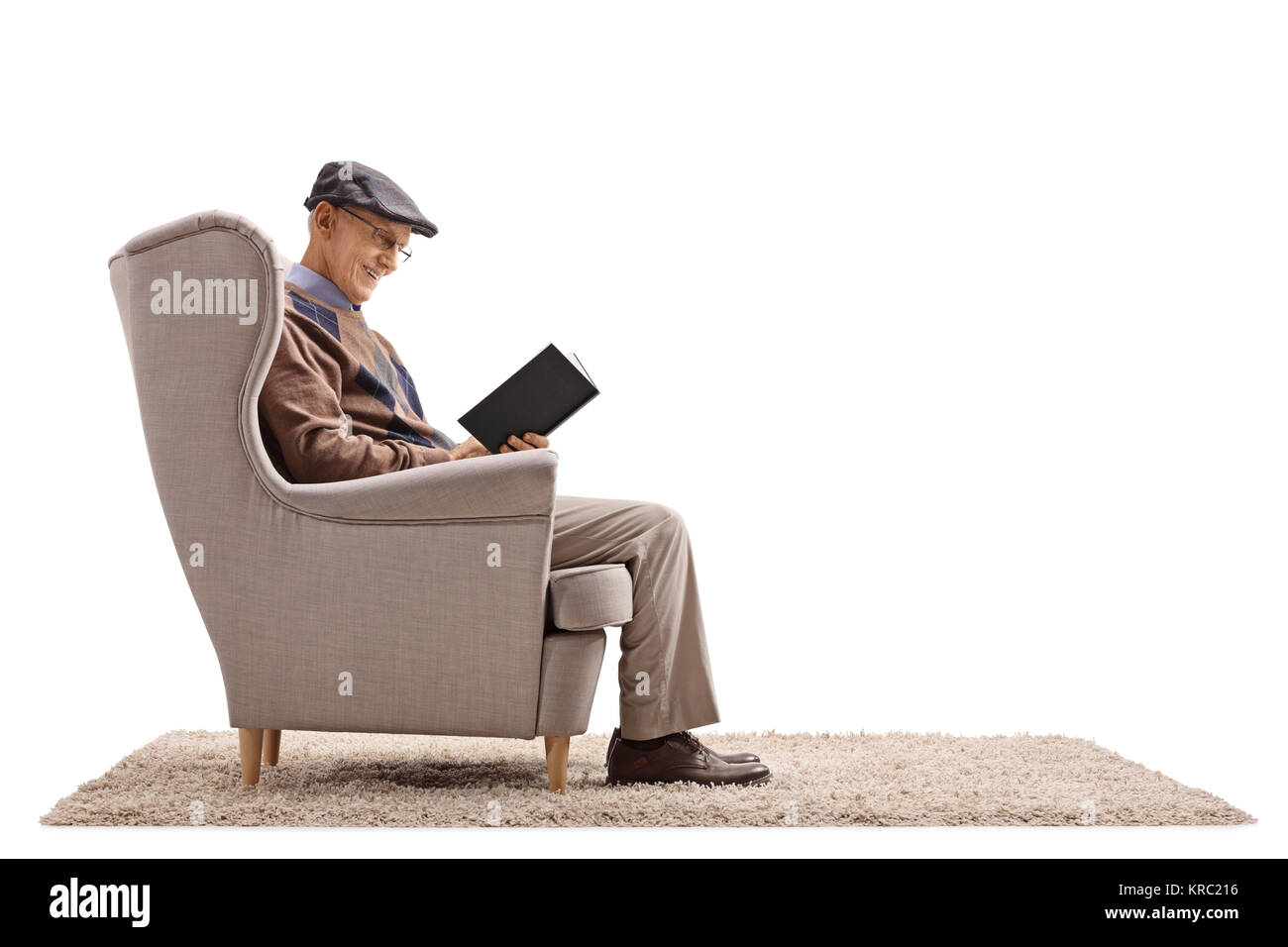 Elderly man seated in an armchair reading a book isolated on white