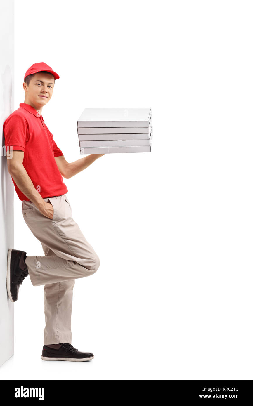 Full length portrait of a teenage pizza delivery guy with a stack of pizza boxes leaning against a wall isolated on white background Stock Photo