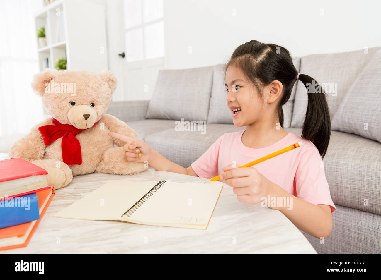 happy lovely girl children teaching her teddy toy learning english at home when she doing school homework in living room. Stock Photo