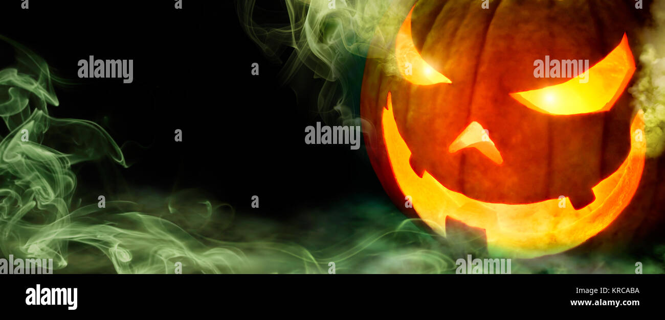 Jack o lantern with evil glowing eyes emanating green smoke, on black panoramic background with copyspace Stock Photo