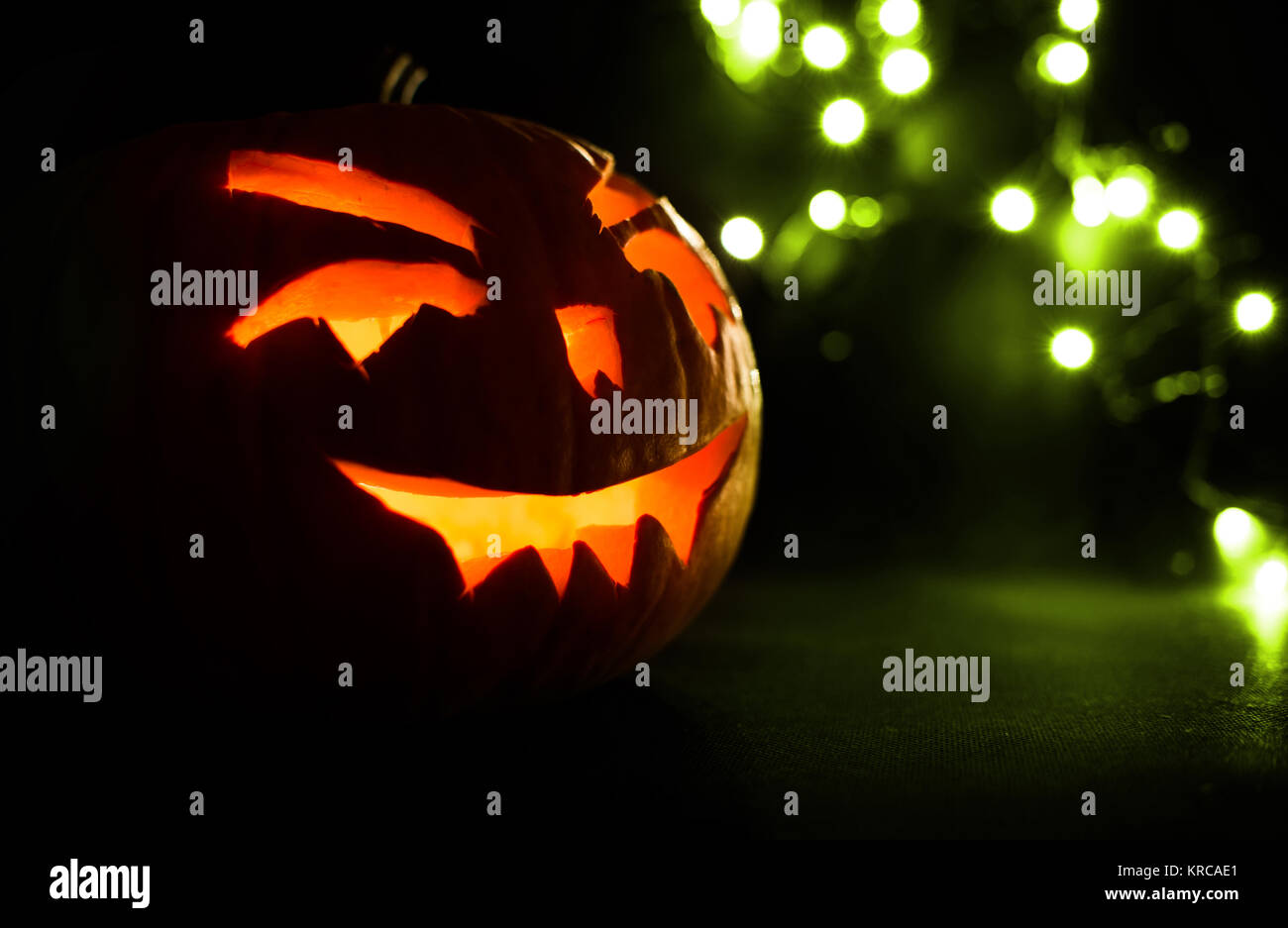 carved face of pumpkin glowing on halloween on green bokeh light ...