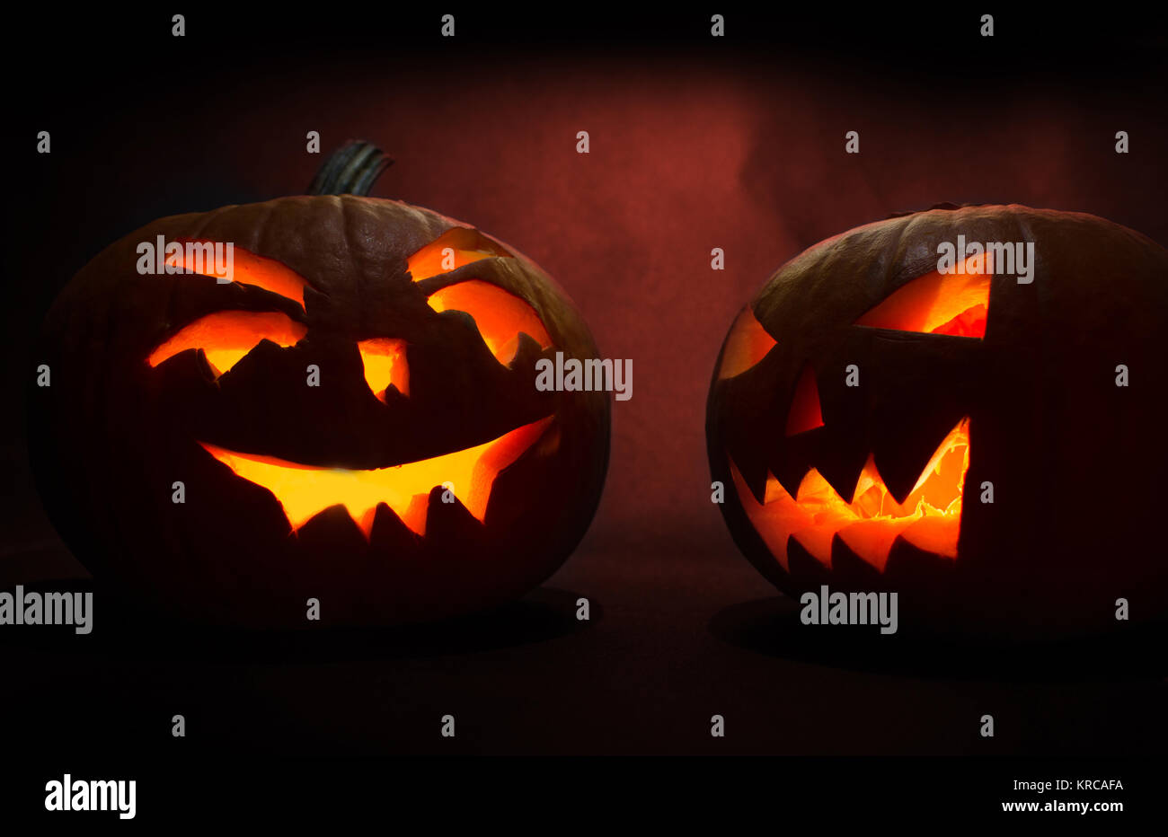 two carved faces of pumpkins glowing on halloween on red background ...