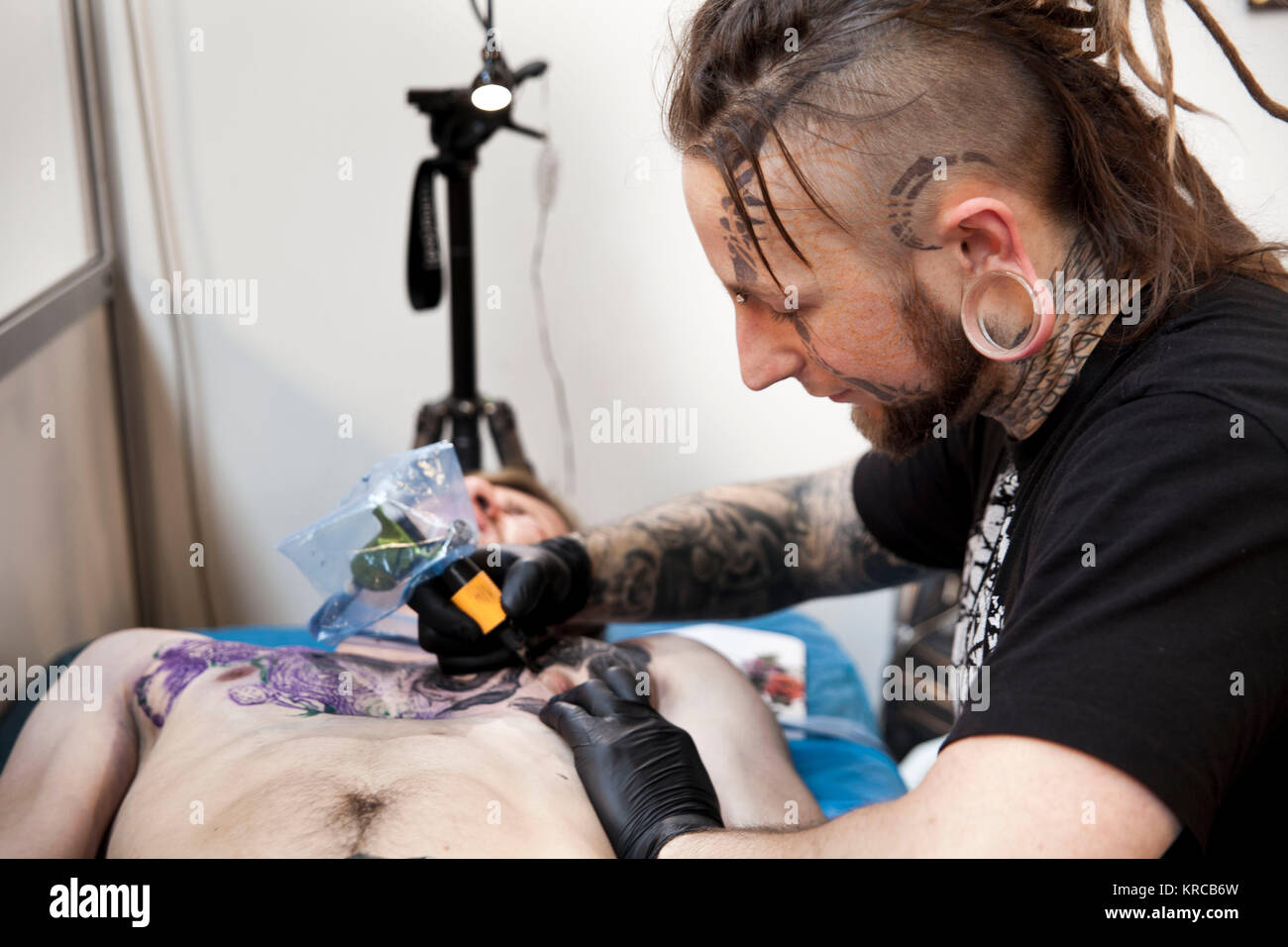 A guest is having a painful chest tattoo at the annual tattoo convention Copenhagen Ink Festival. The audience can be tattooed directly at the festival by booking a time with their favorite artist. Denmark 2013 Stock Photo
