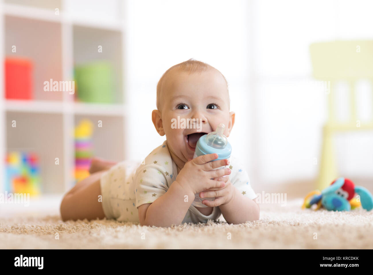 Pretty baby boy drinking water from bottle. Smiling child is 7 months old. Stock Photo