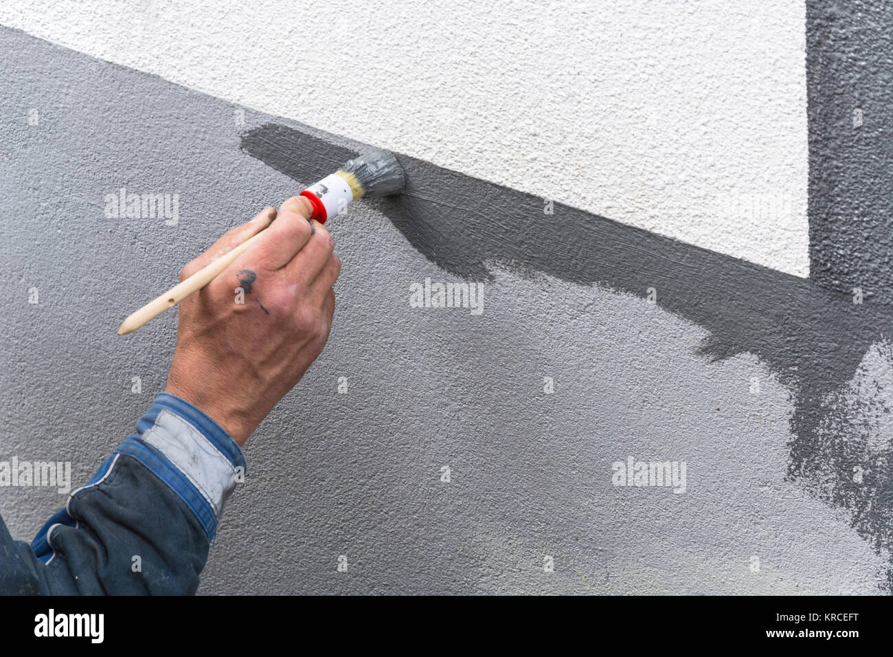 Nahaufnahme Arm eines Anstreicher mit Farbrolle in der Hand streicht eine Hauswand mit grauer Farbe. Stock Photo