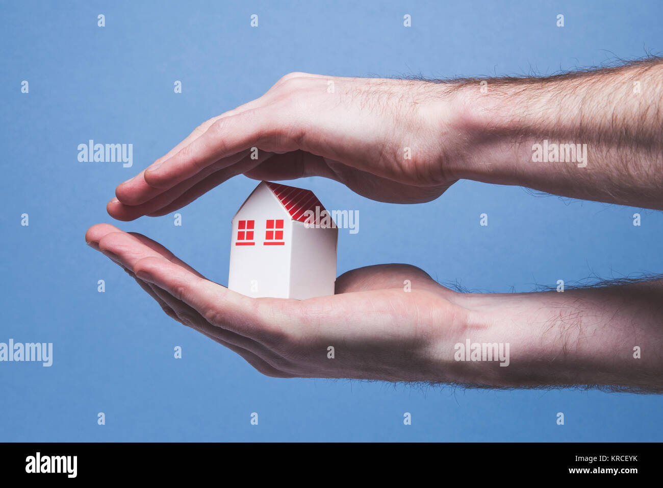 Hands covering a toy house. Home protection concept Stock Photo