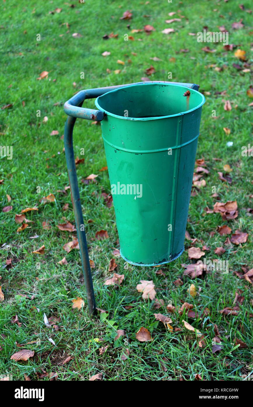 Green partially rusted metal public trash can surrounded with green