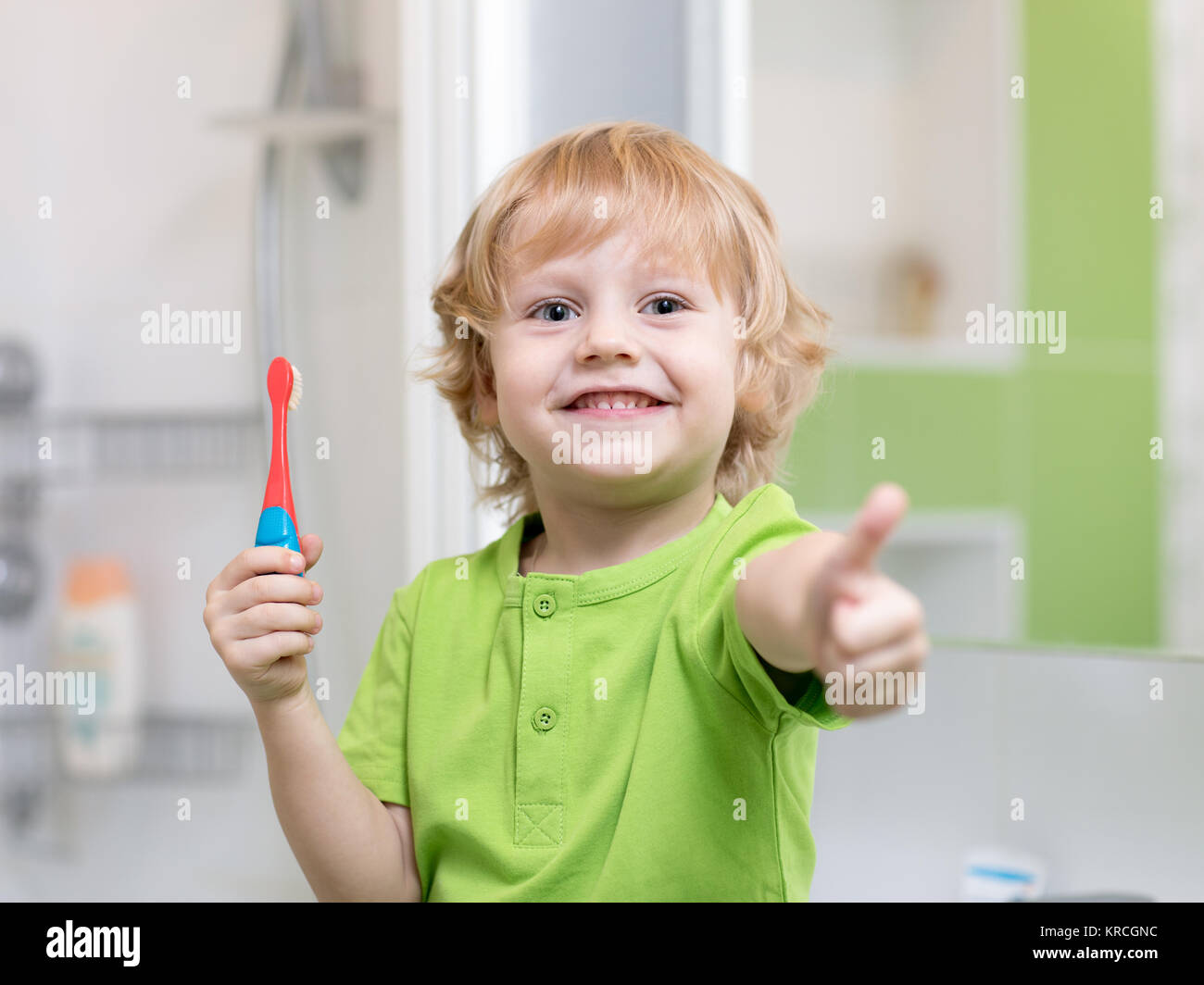 Little kid boy brushing his teeth in the bathroom. Smiling child holding toothbrush and showing thumbs up. Stock Photo