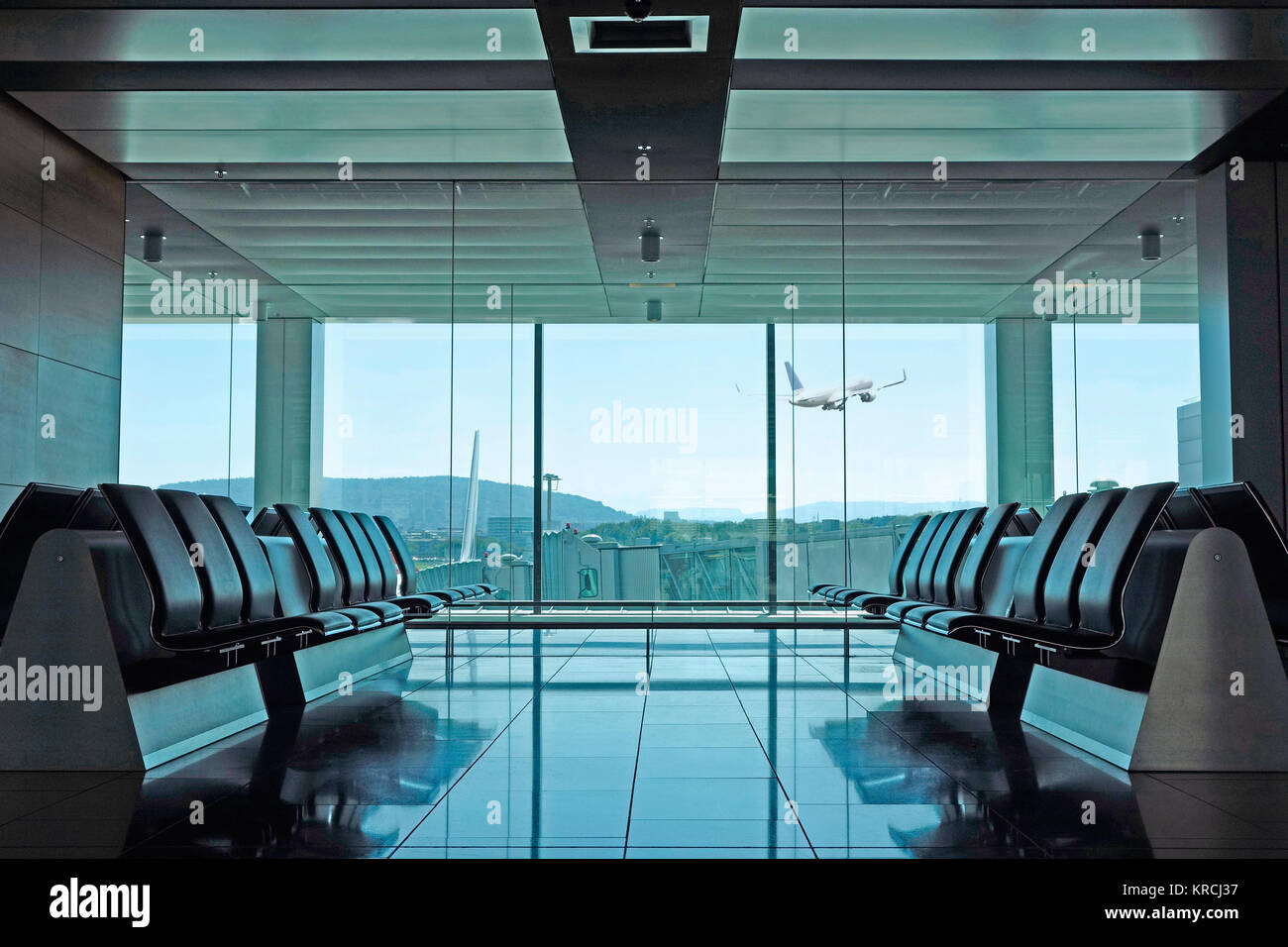 An empty modern airport departure lounge with seating and plane taking off in the background Stock Photo