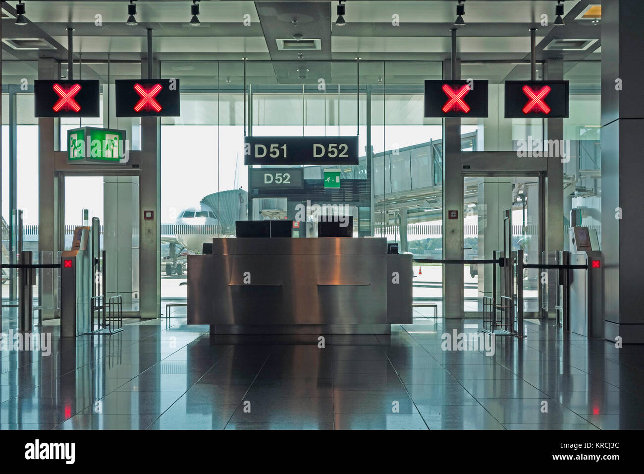 Modern airport departure check in gates closed with red X signs above and an aircraft on the runway. Stock Photo