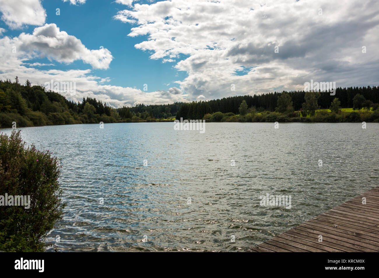 Lonely lake with reflections in the water and forests around and blue sky with clouds Stock Photo