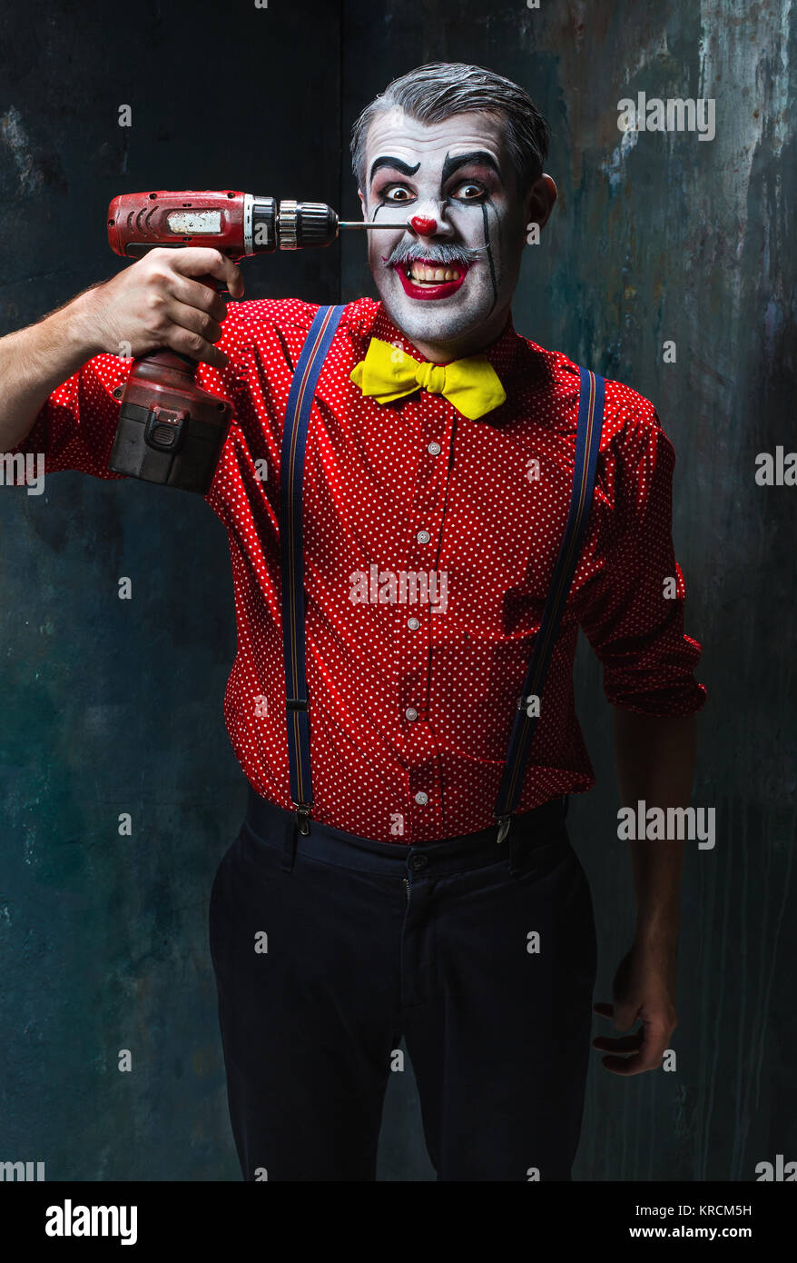 The scary clown and electric drill on dack background. Halloween concept Stock Photo
