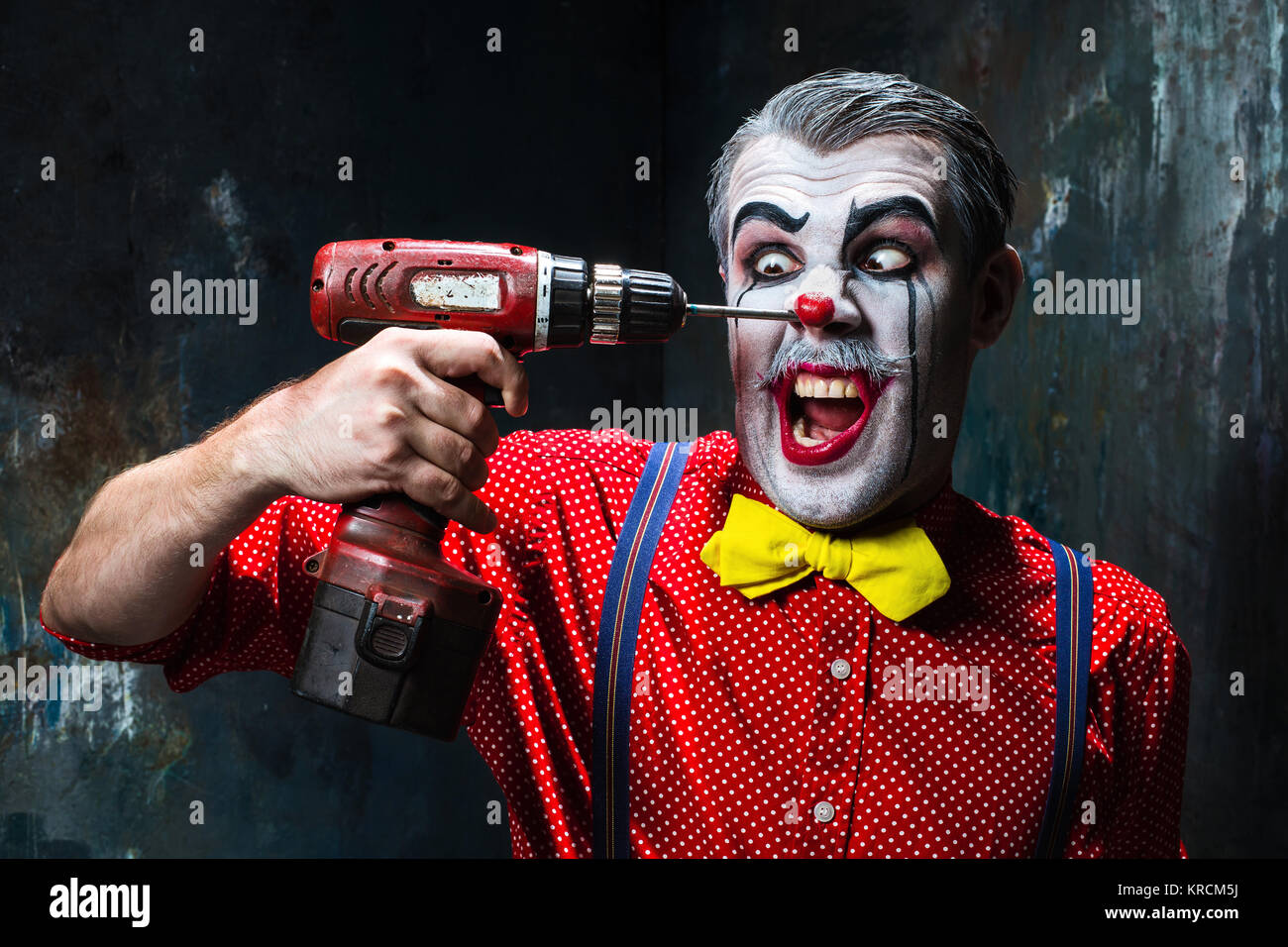 The scary clown and electric drill on dack background. Halloween concept Stock Photo