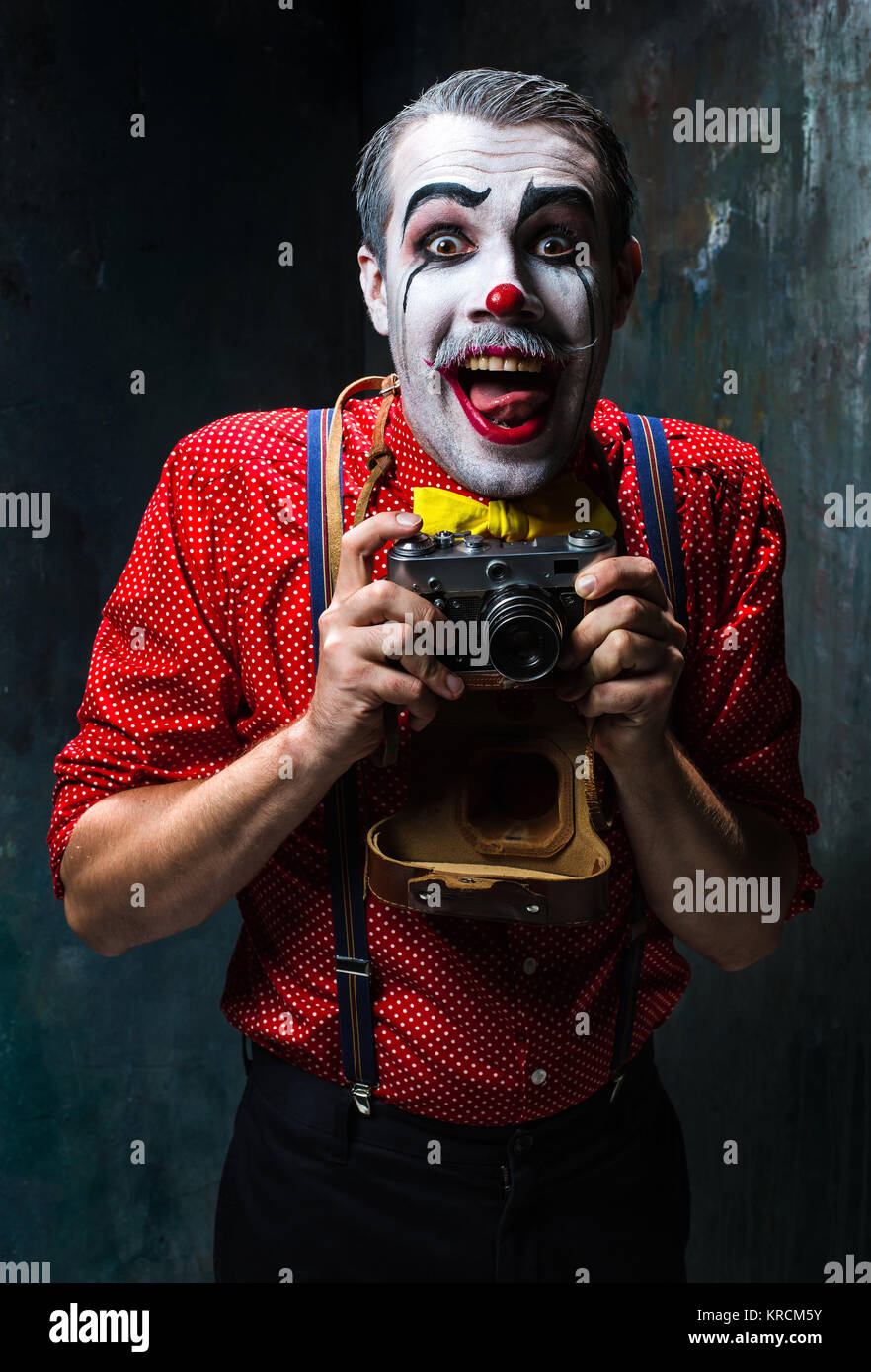 The scary clown and a camera on dack background. Halloween concept Stock Photo