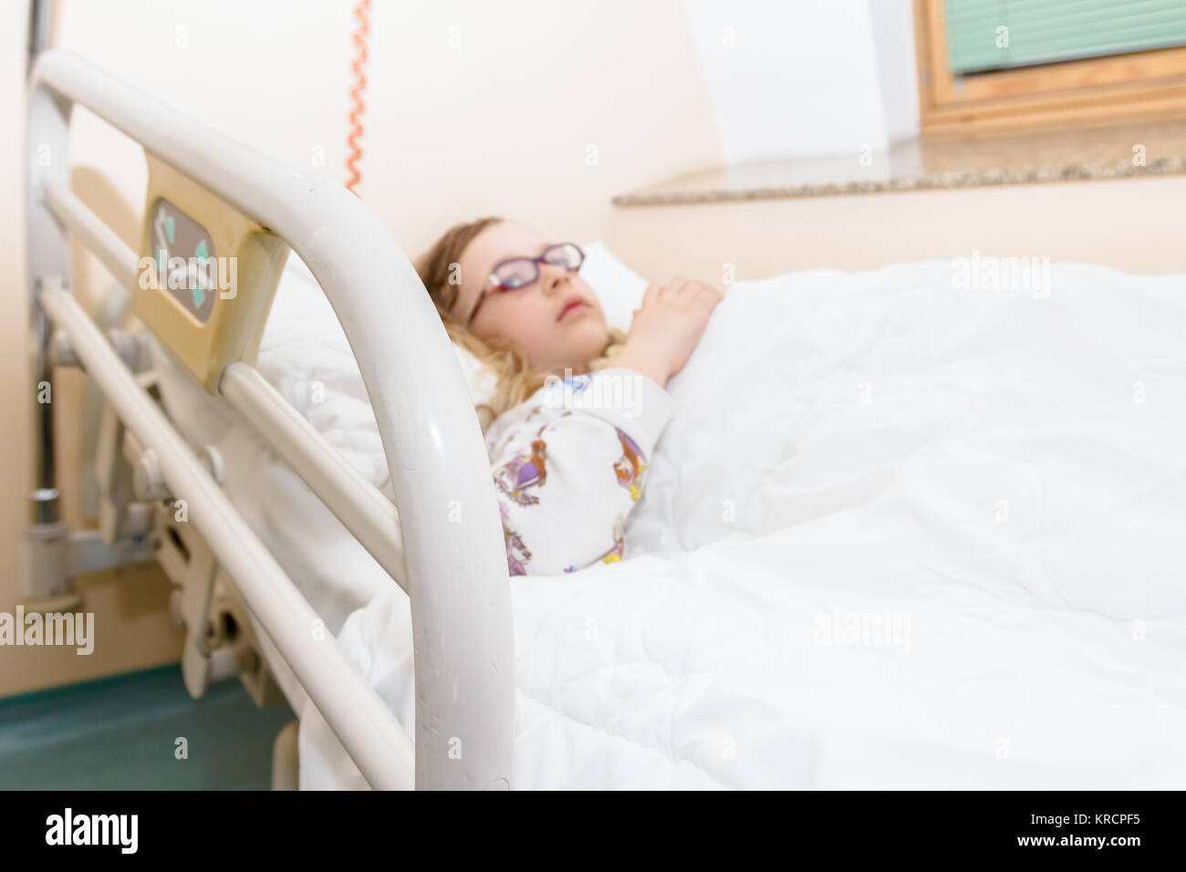 Little girl is resting in a hospital bed with her teddy bear, clinic hospitalization. Stock Photo