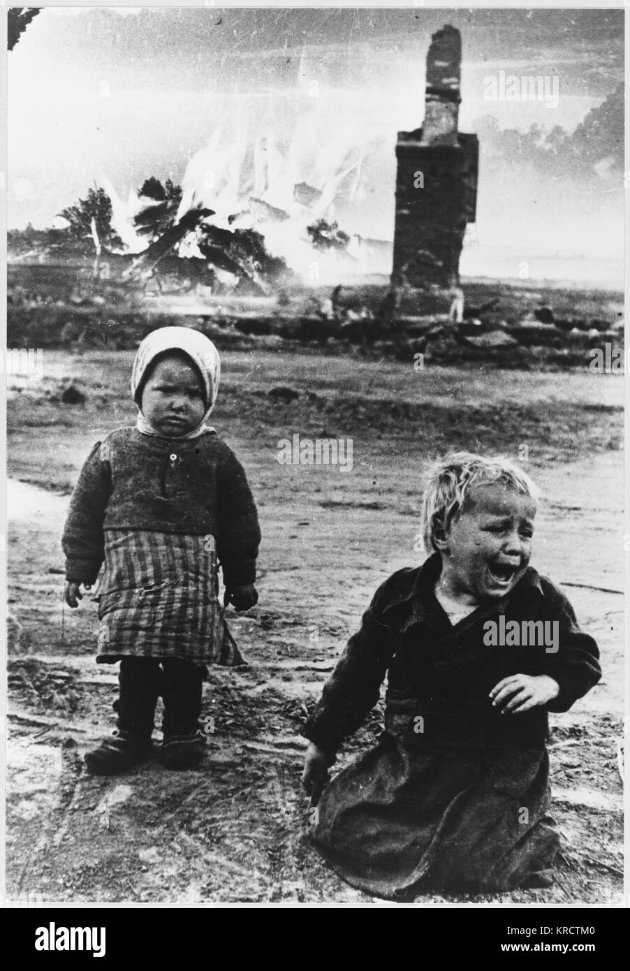Two Orphaned children wander alone among the smouldering ruins of their town Stock Photo
