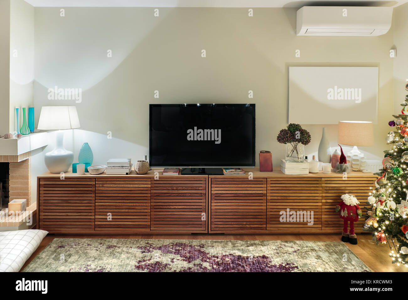 A modern large wooden cabinet with a flat TV placed on a living room with a christmas tree. Stock Photo