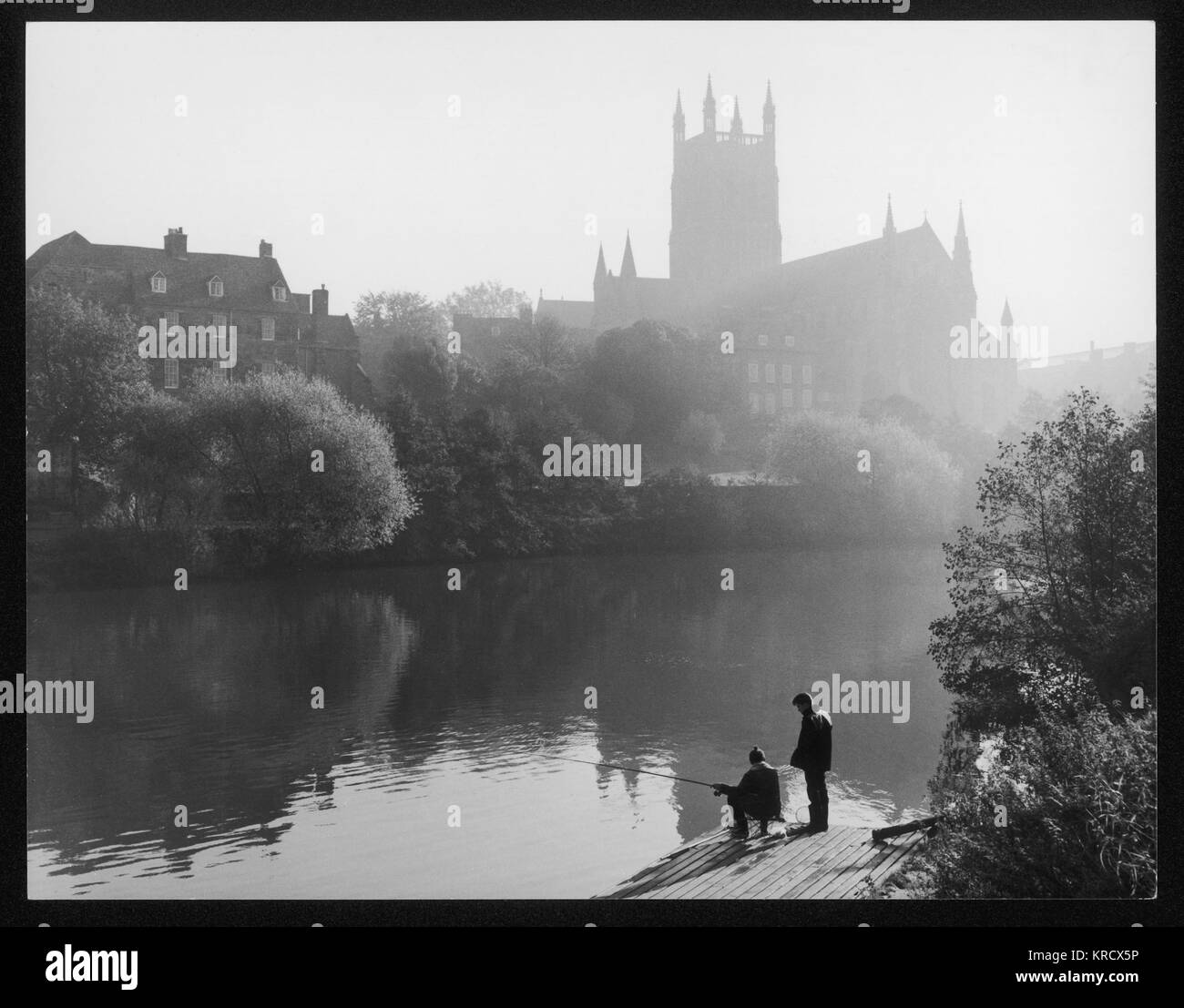 Angling in the River Severn on a misty morning, while  the sun rises behind  Worcester Cathedral in the  distance.      Date: 1960s Stock Photo