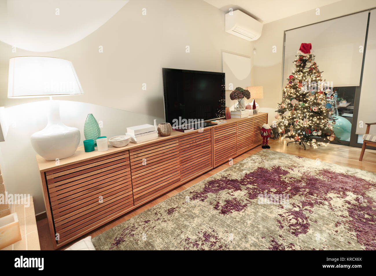 A modern large wooden cabinet with a flat TV placed on a living room with a christmas tree. Stock Photo