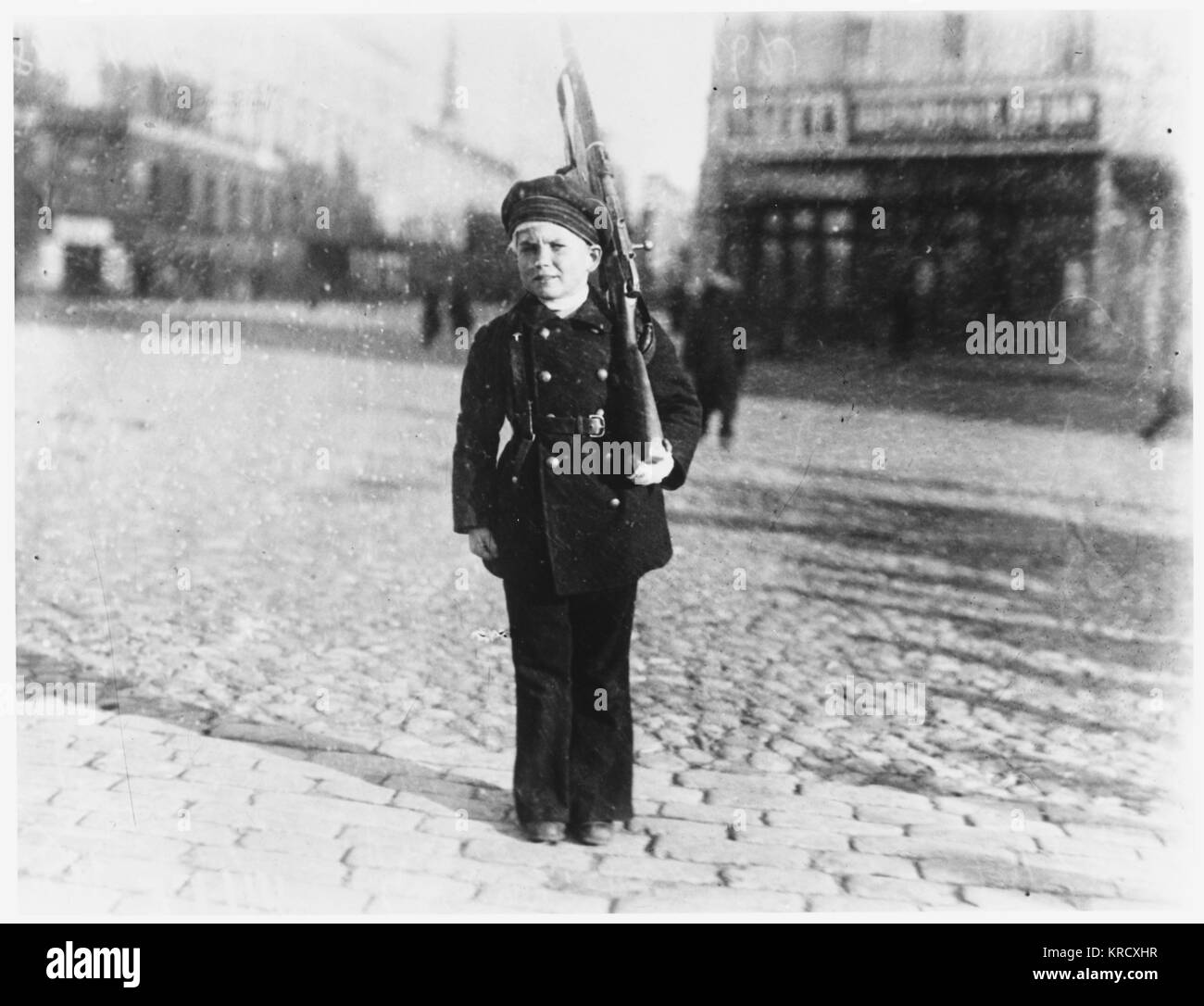 A young Russian boy is dressed  as a defender of Petrograd, in  a uniform with a rifle         Date: 1919 Stock Photo