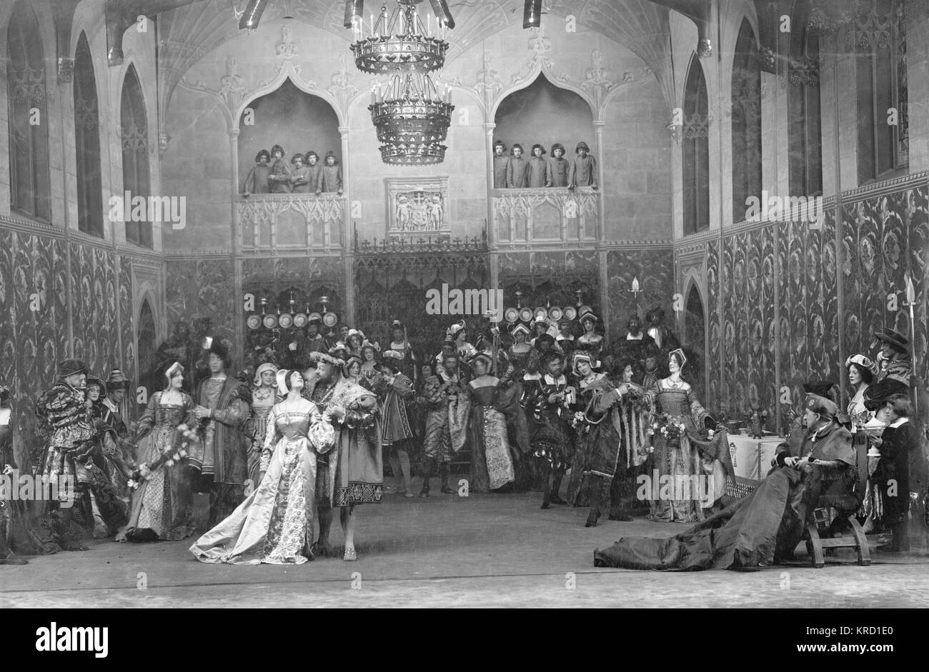 A scene from Shakespeare's play, Henry VIII, in a production by Herbert Beerbohm Tree at His Majesty's Theatre, London.  The production opened in 1910, was revived for the London Shakespeare Festival in 1911, and was repeated again in 1912.  Tree played Cardinal Wolsey.  Other actors were Violet Vanbrugh (Queen Katherine), Arthur Bourchier (King Henry) and Laura Cowie (Anne Bullen).  This scene shows Henry and Anne in conversation, with the rest of the court looking on and gossipping.  Wolsey sits in a chair on the far right.   (1 of 6)       Date: circa 1910-1912 Stock Photo