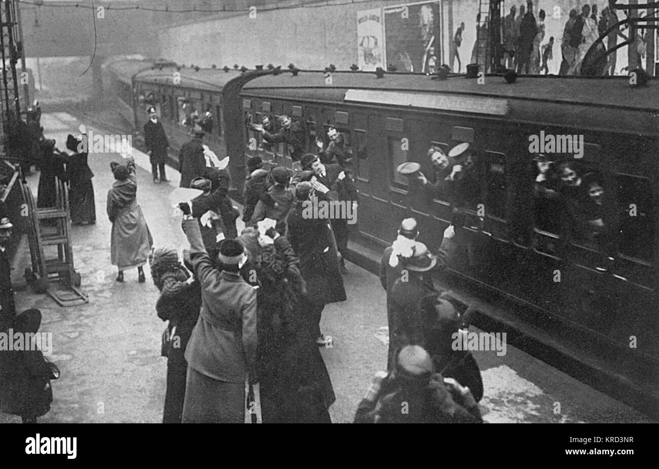 Troops arriving (or possibly departing) at an unidentified London rail station during the First World War.  Numerous women and family members stand on the platform bidding farewell, and on the hoardings seen above the train are recruitment posters.     Date: 1914 Stock Photo