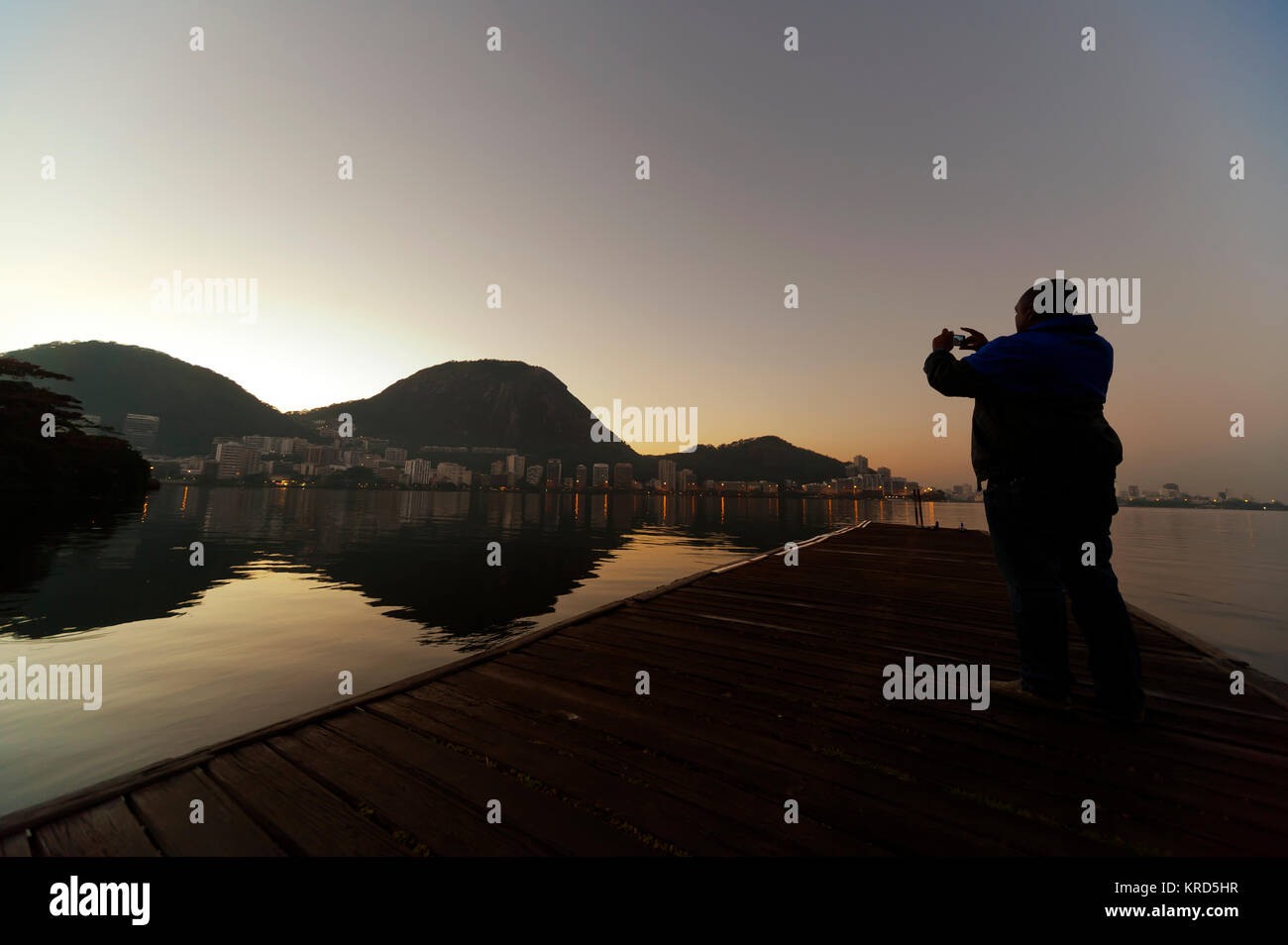 A man using his cellphone to take pictures early morning at Rodrigo de Freitas Lagoon, Rio de Janeiro, Brazil Stock Photo