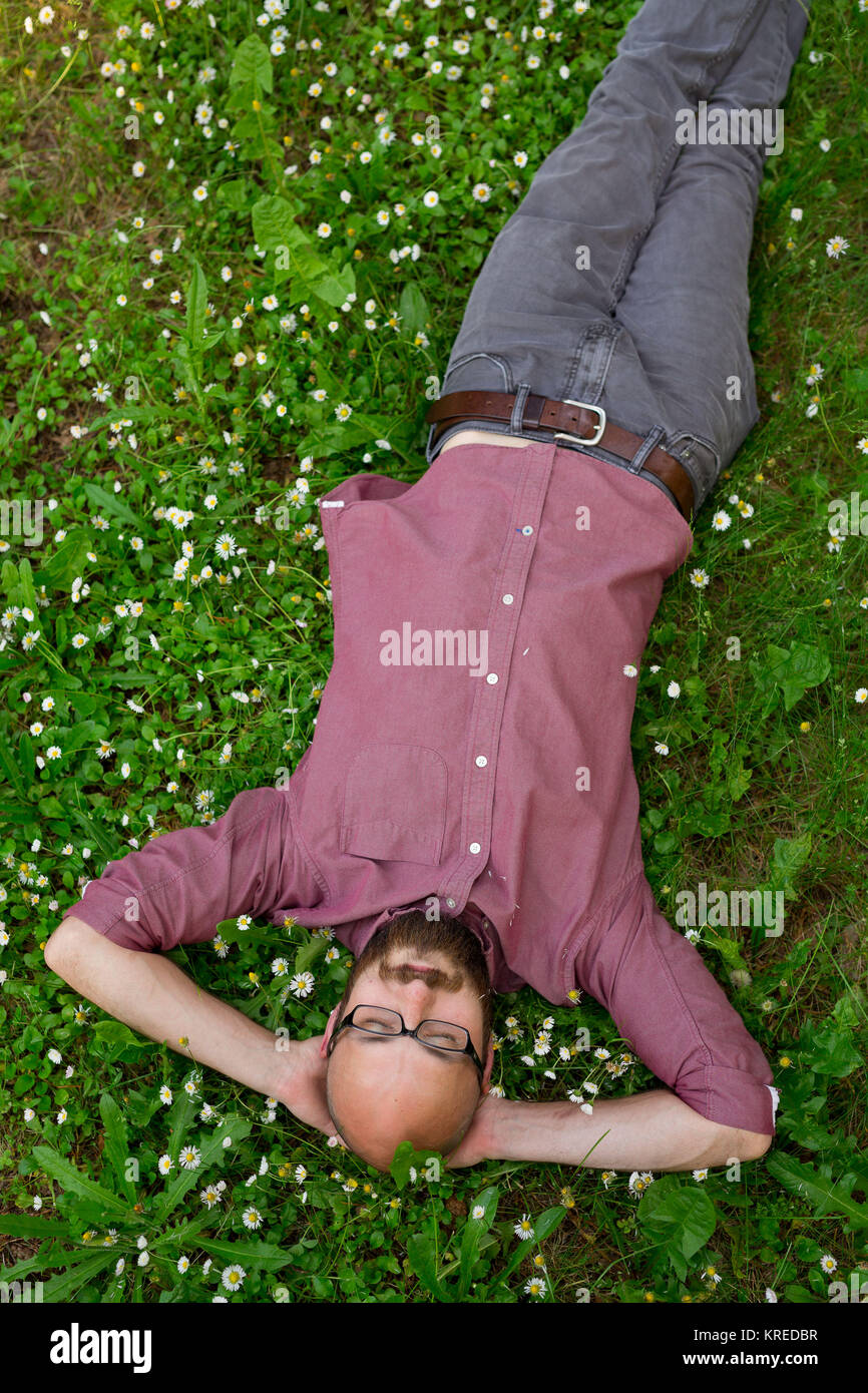 Bald man puts his arms behind his head to relax on some green grass in the Summer in Oregon at a park. Stock Photo