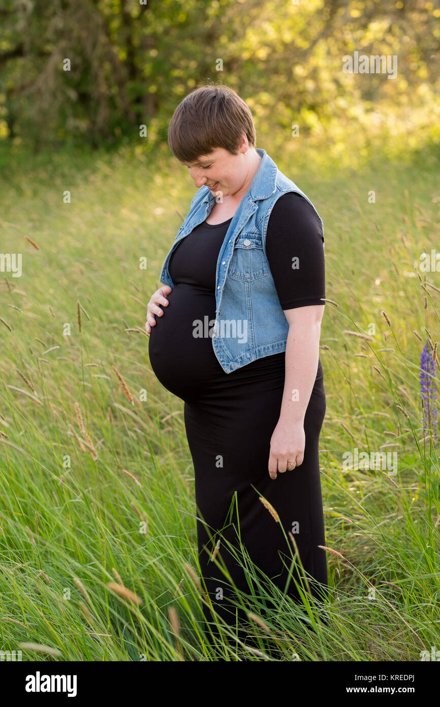 Maternity photo of a young woman with a short hair pixie cut in her third trimester with child. Stock Photo