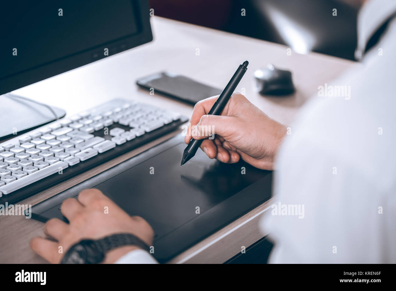 Graphic designer's workspace. Hand on pen tablet. Young smart man in the office. Free black monitor copy space for design. Warm glare of sun light. Stock Photo