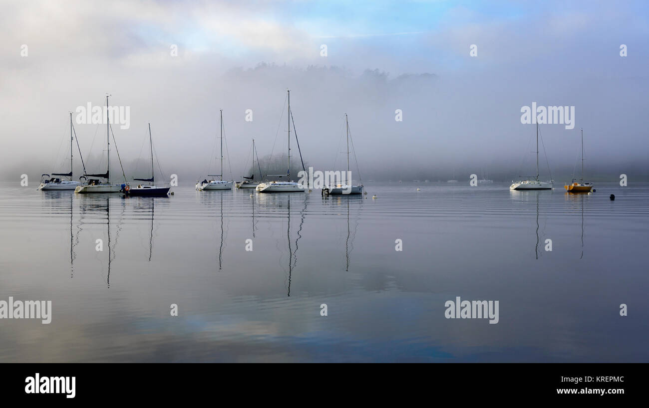 Boats on their moorings on Windermere as the sun starts to lift the early morning mist Stock Photo