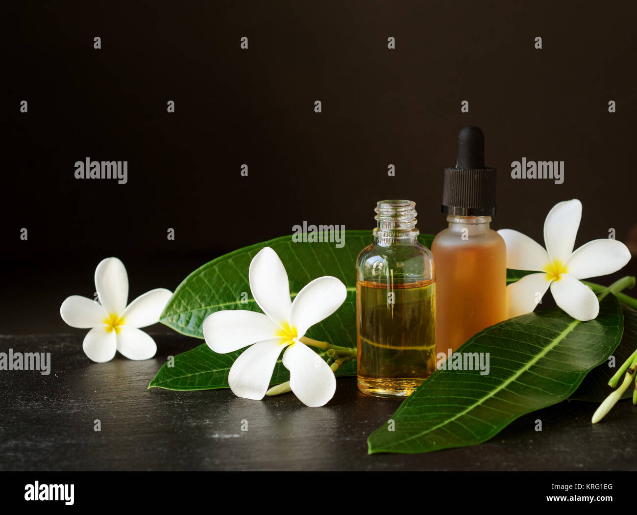 small glass jars with oil and Frangipani Plumeria patchouli flowers for spa treatments on a black background, selective focus Stock Photo